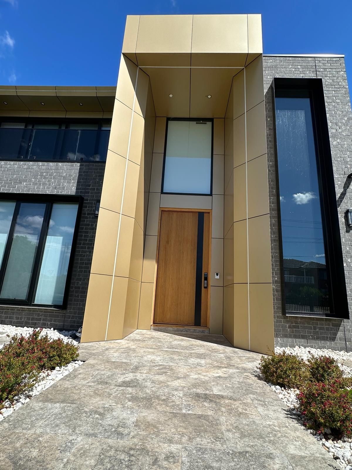 Modern house entrance with tan stone portal, wood front door, and tall black-framed windows