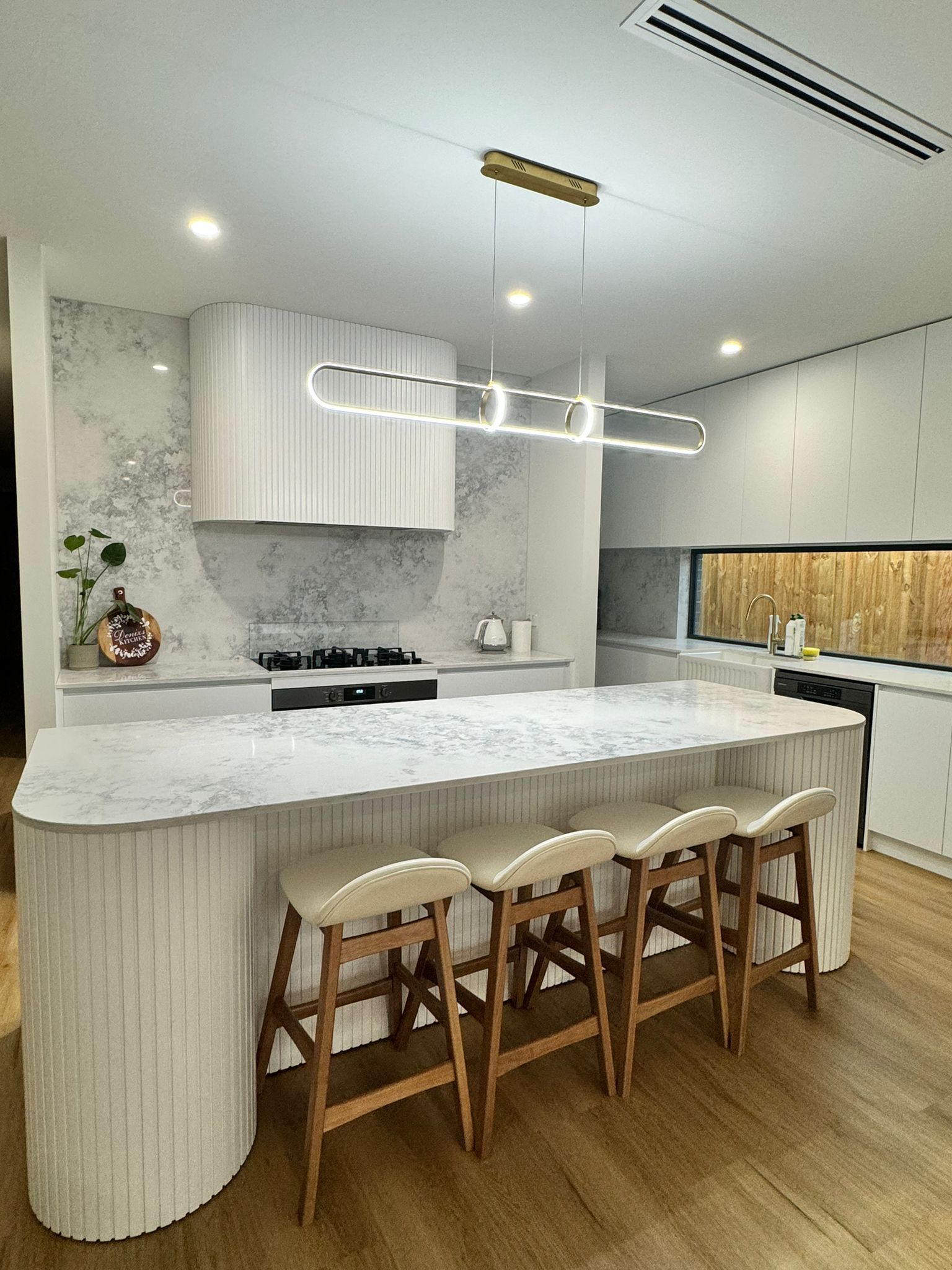 Modern kitchen with marble island, wooden stools, white cabinets, and warm wood flooring
