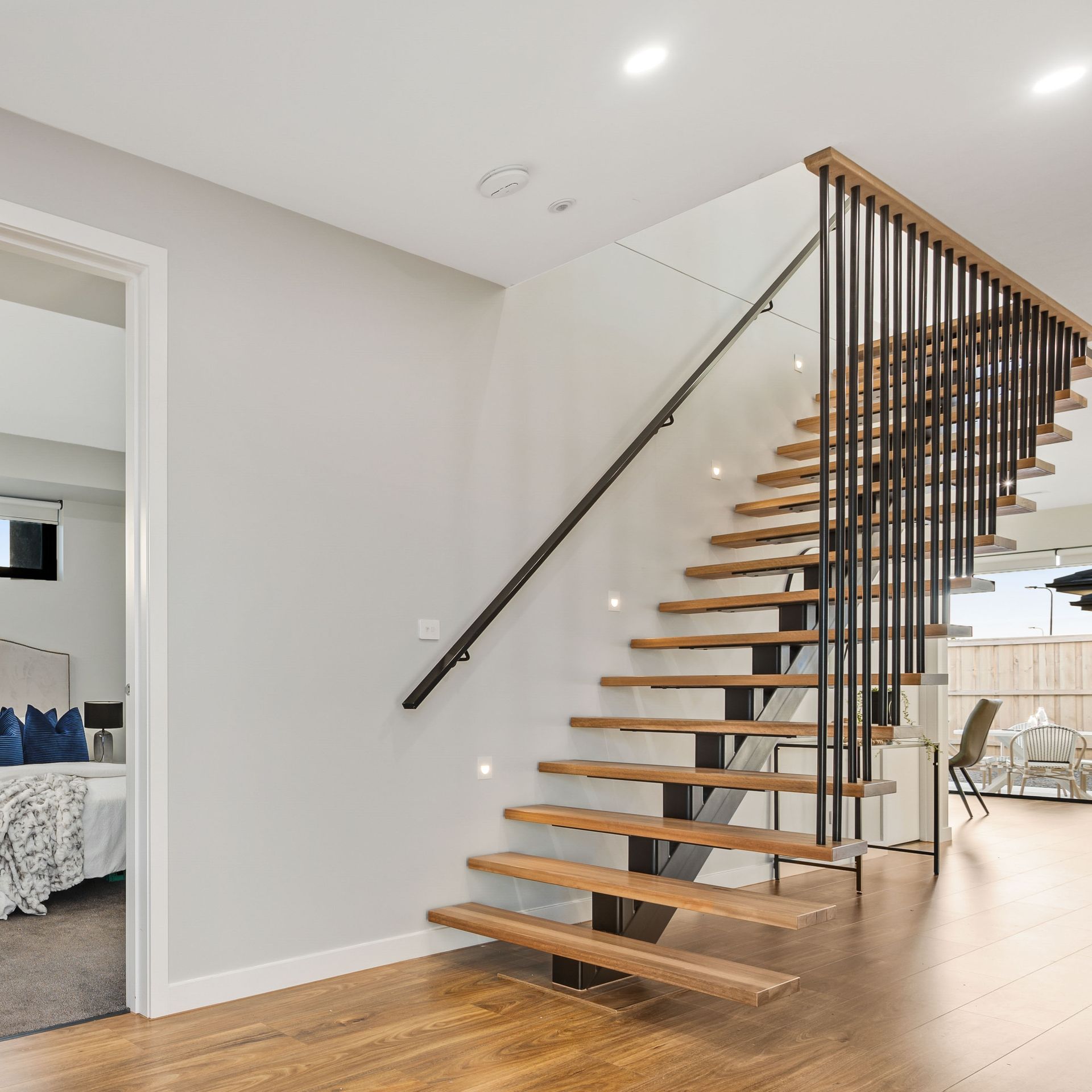 Modern staircase with wooden floating steps, black railing, and bright open interior with hardwood floors
