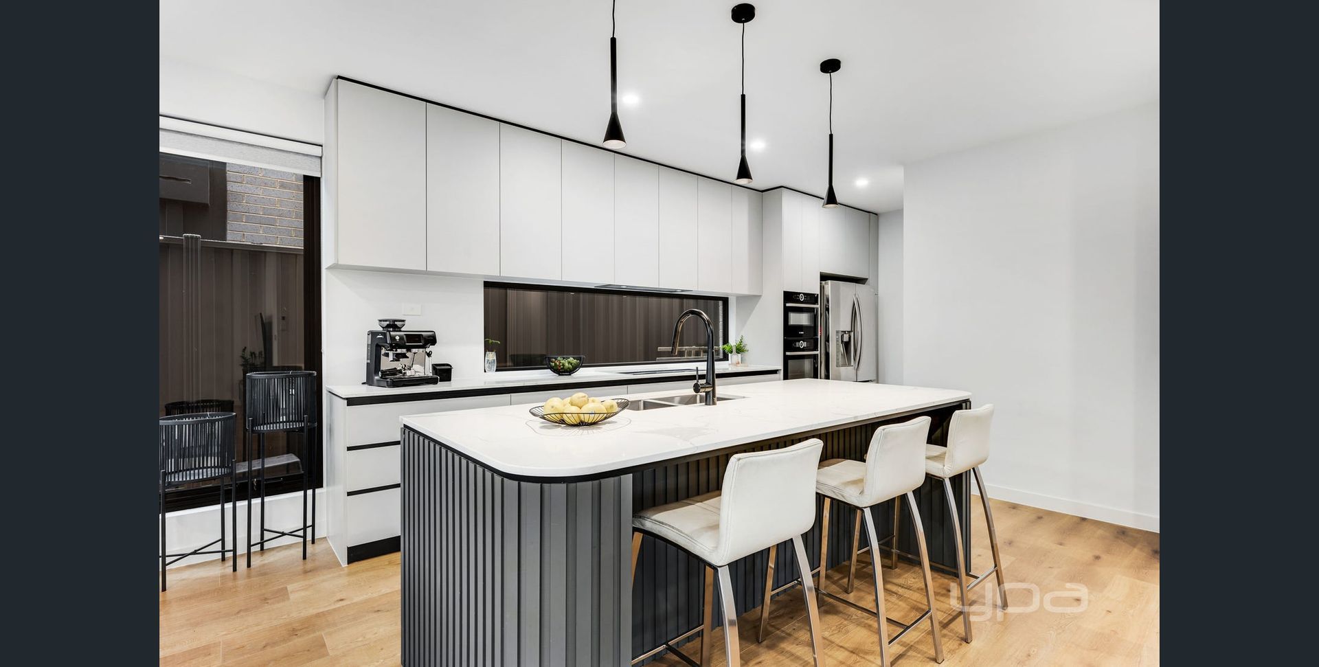 Modern white kitchen with black island, pendant lights, and bar stools