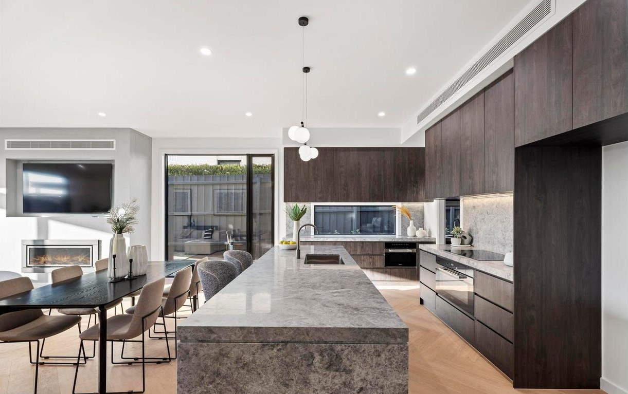 Modern open-plan kitchen and dining area with dark wood cabinets, marble island, and large glass doors