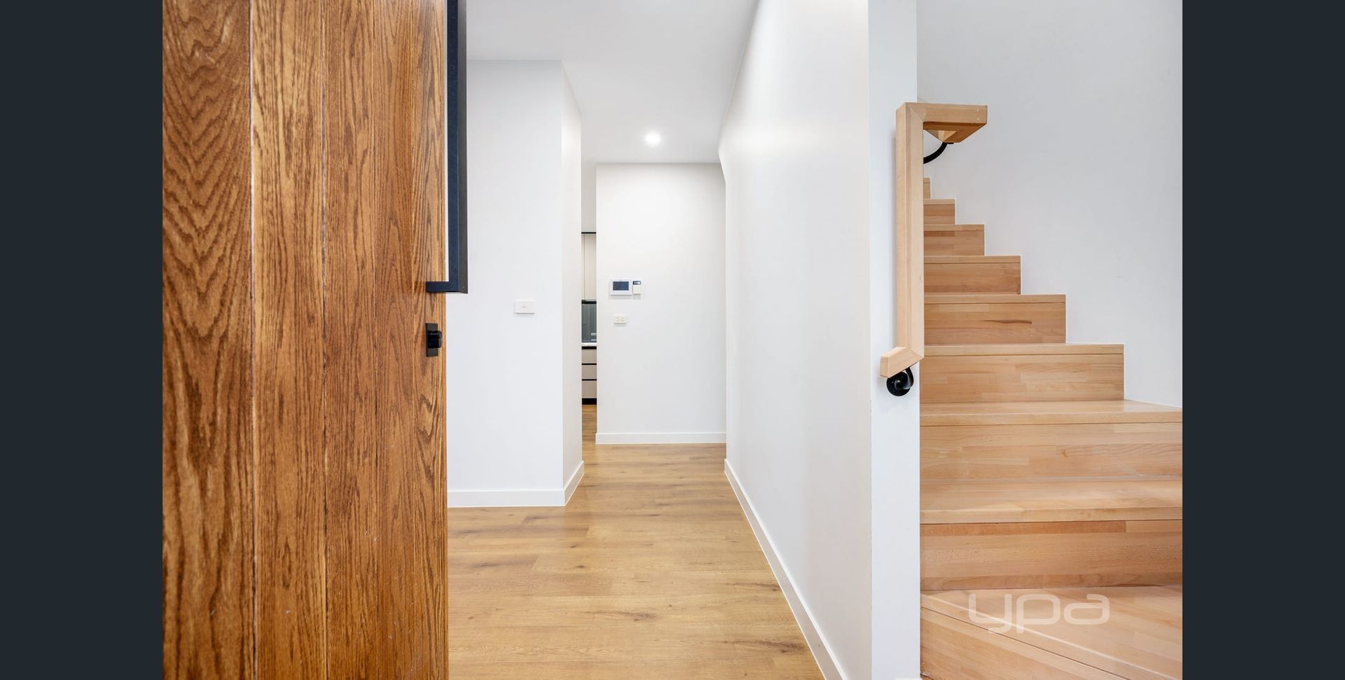 Modern hallway with wood floor, white walls, a large wooden door, and stairs on the right