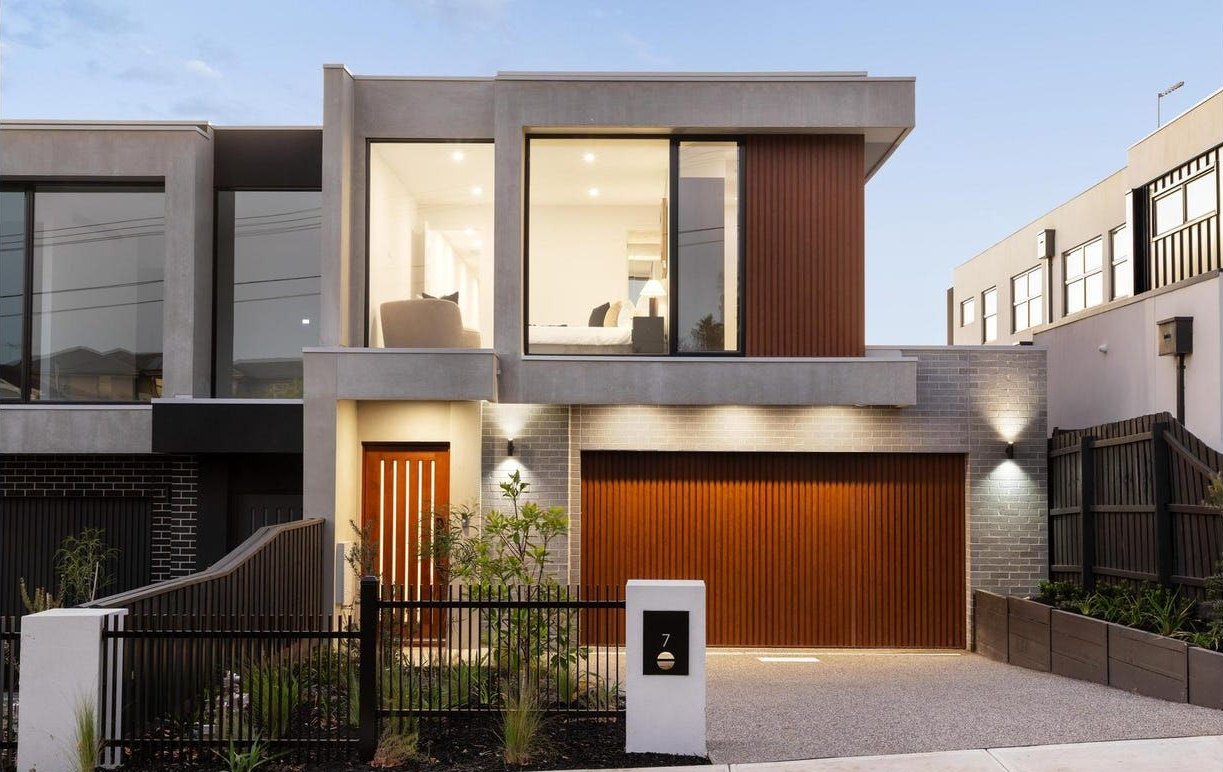 Modern two-story house with large windows, wood accents, and a small front garden at dusk