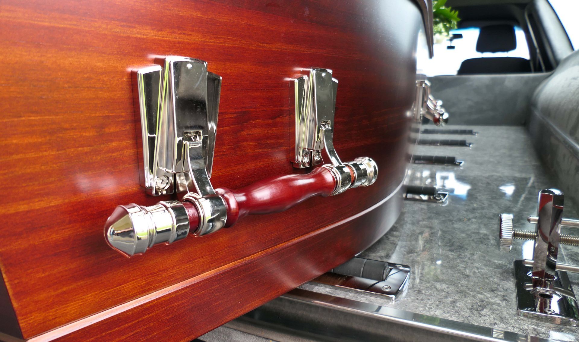 Primo piano di una bara di legno marrone con maniglie d'argento all'interno di un carro funebre.