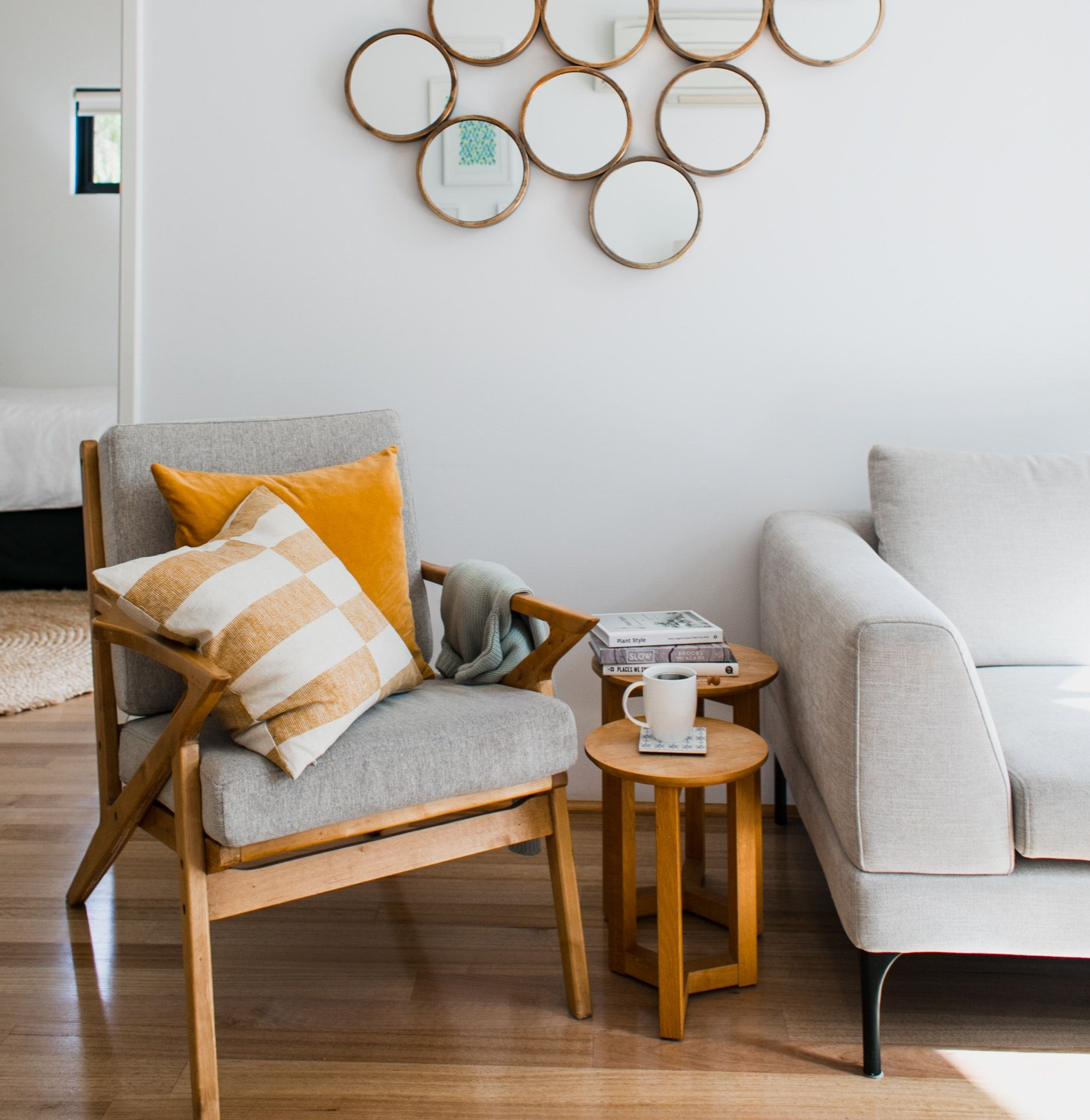 Living room with wood floors, gray chair, white sofa, round side tables, and circular mirrors on the wall.