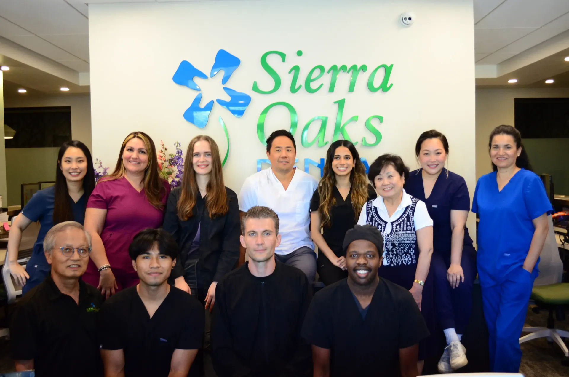 Staff of Sierra Oaks dental practice smiling in front of logo on a wall.