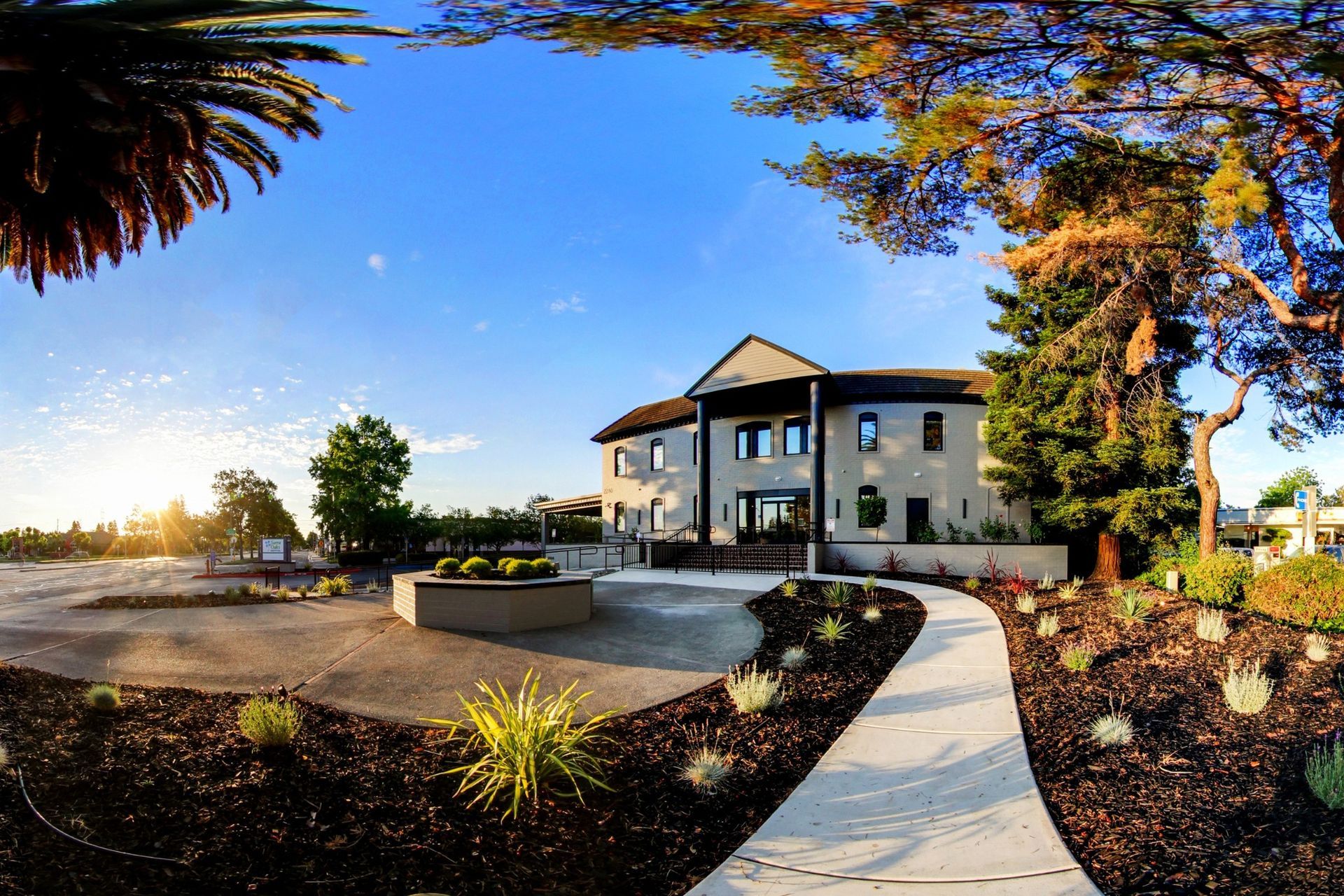 Elegant two-story building with a winding path, surrounded by landscaping, under a blue sky.