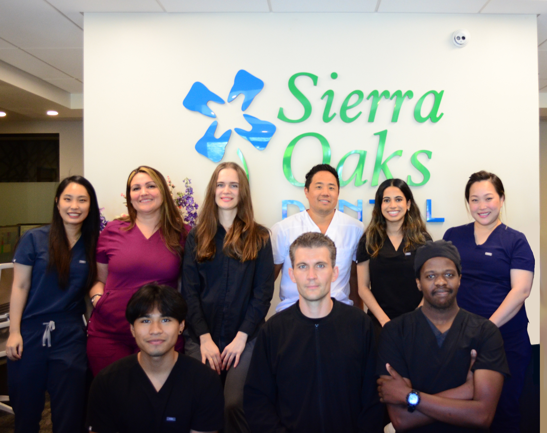 Staff of Sierra Oaks dental practice smiling in front of logo on a wall.