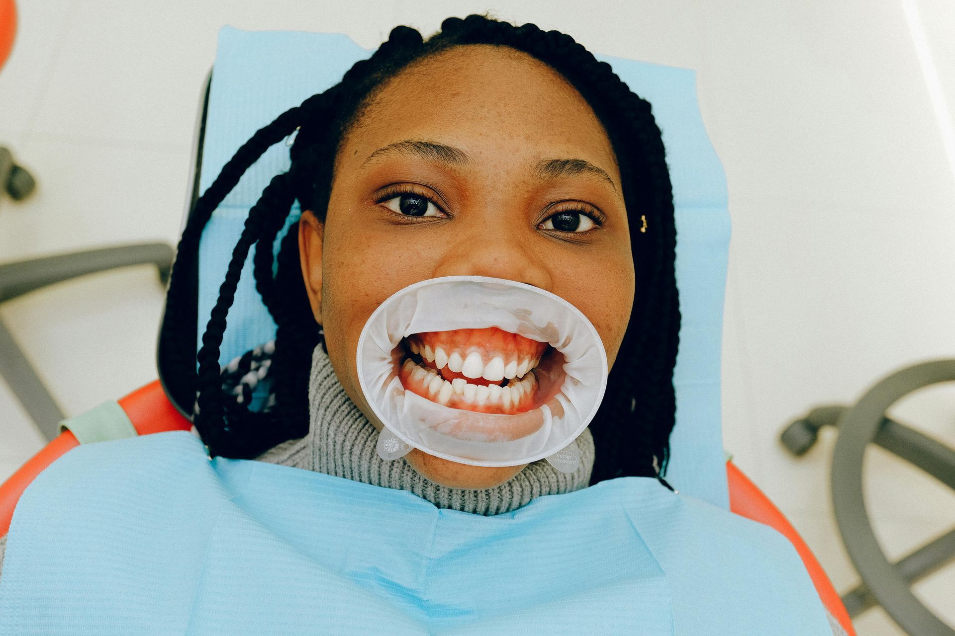 Person in dentist chair with a mouth retractor, open mouth, light blue sheet.