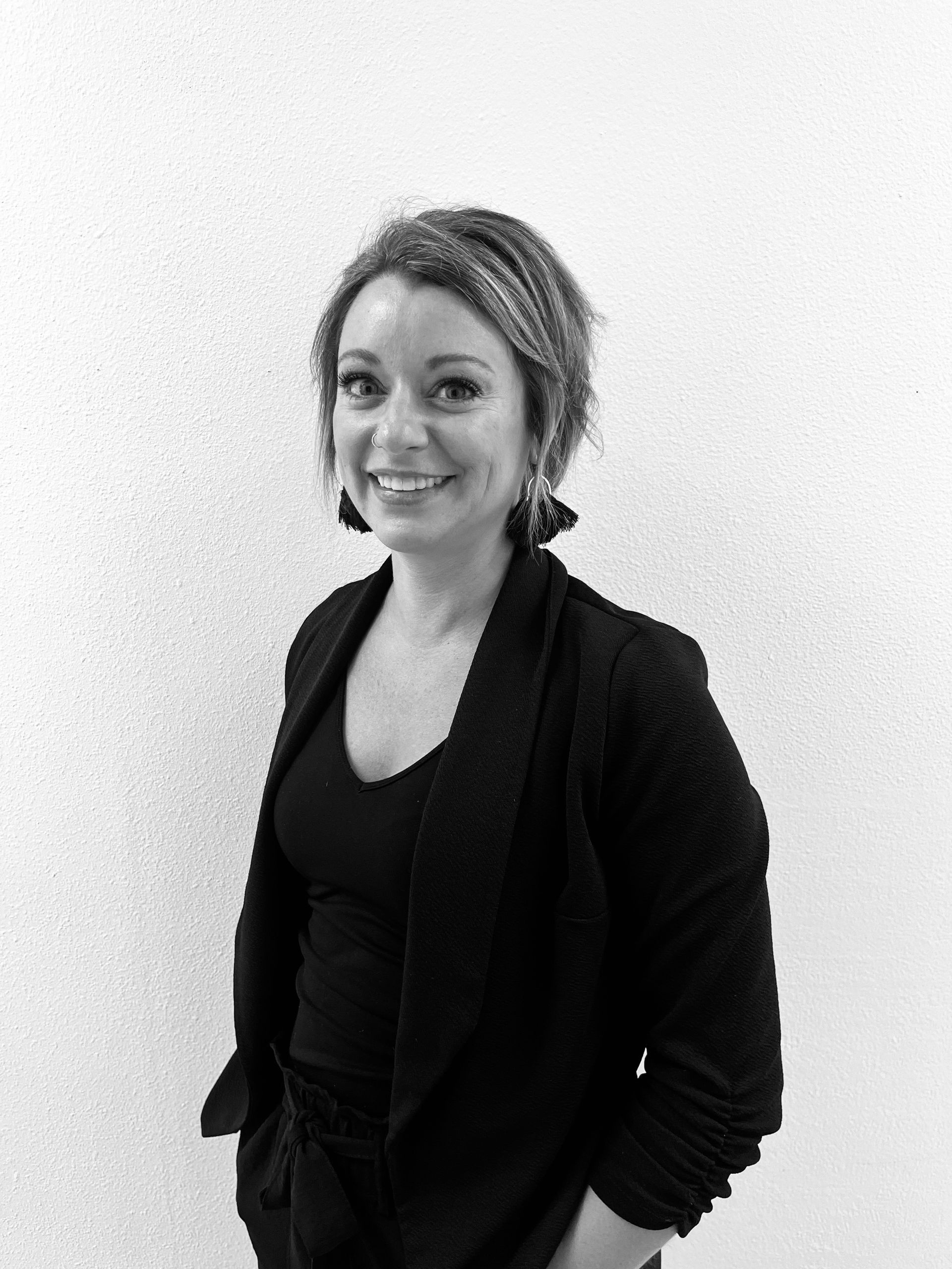 Smiling person in black jacket standing against a plain white wall