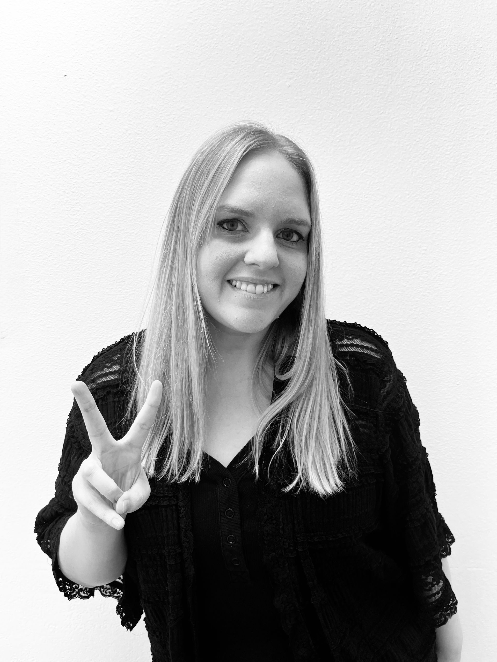 Person smiling and making a peace sign against a plain background