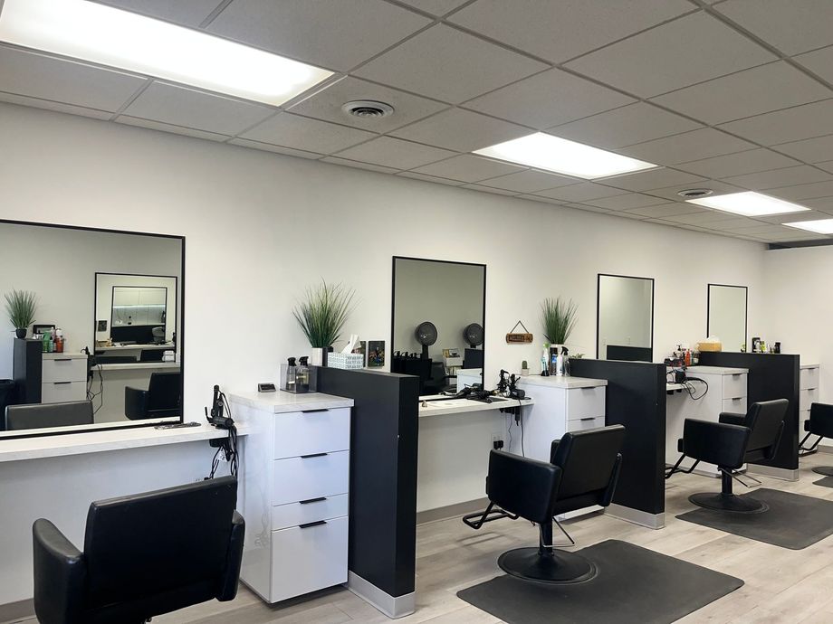 Black salon chair, mirror, and storage unit in a bright, white room with a dark mat.