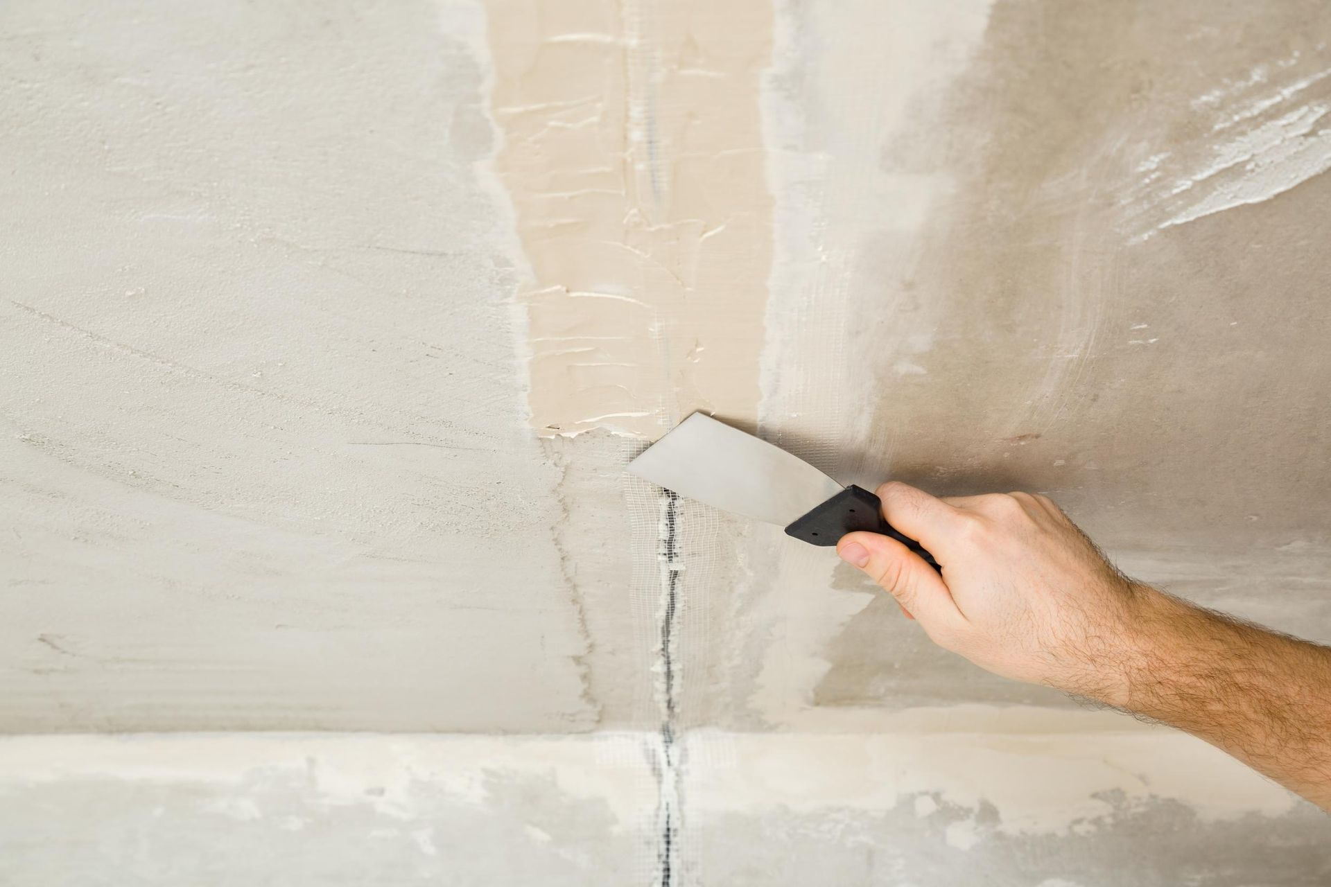 Person using a putty knife to fill a crack in a light-colored ceiling with a spackle.
