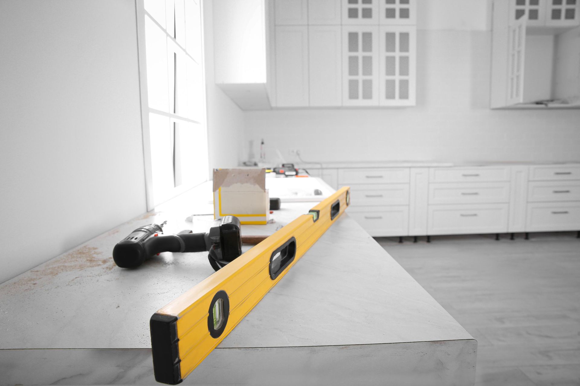 A yellow level and power drill on a countertop in a kitchen undergoing renovation.