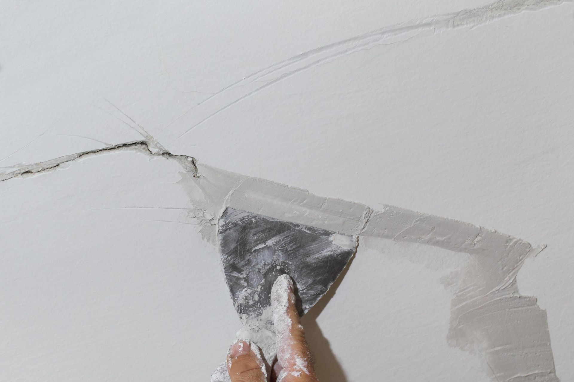 Hand using a putty knife to apply spackle to a crack in a white wall.