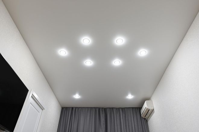 White ceiling with recessed lights, above a room with white walls and curtains.
