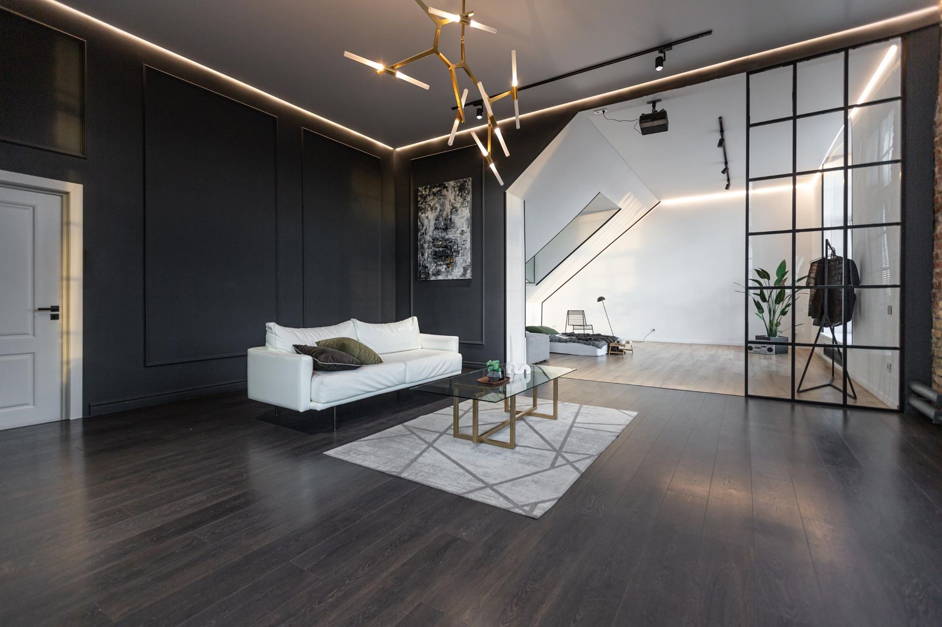Modern living room with dark walls, white sofa, glass partition, and gold chandelier.