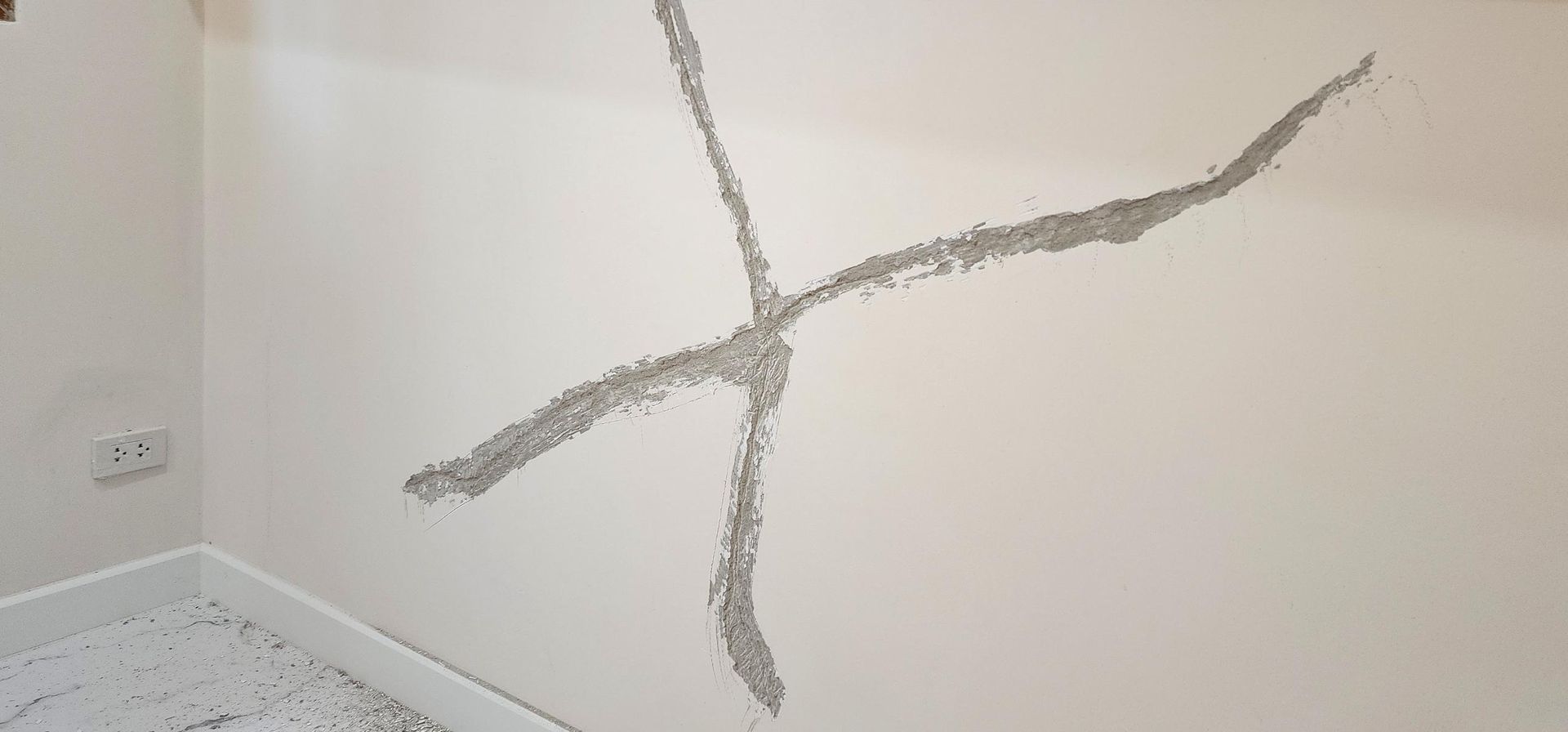 A white wall with a large, patched crack in a cross-like shape.