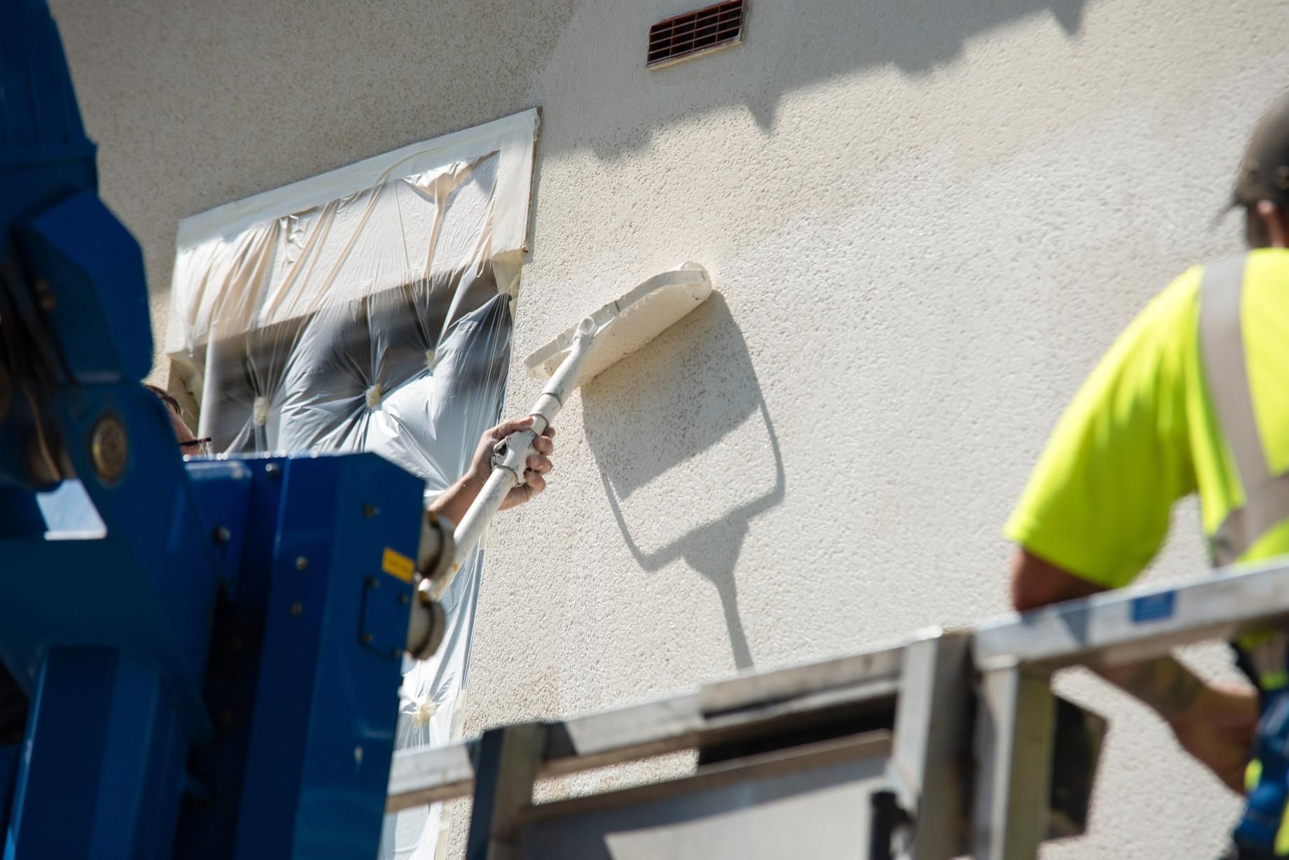 Man applying stucco to a building wall, using a trowel while on a lift.