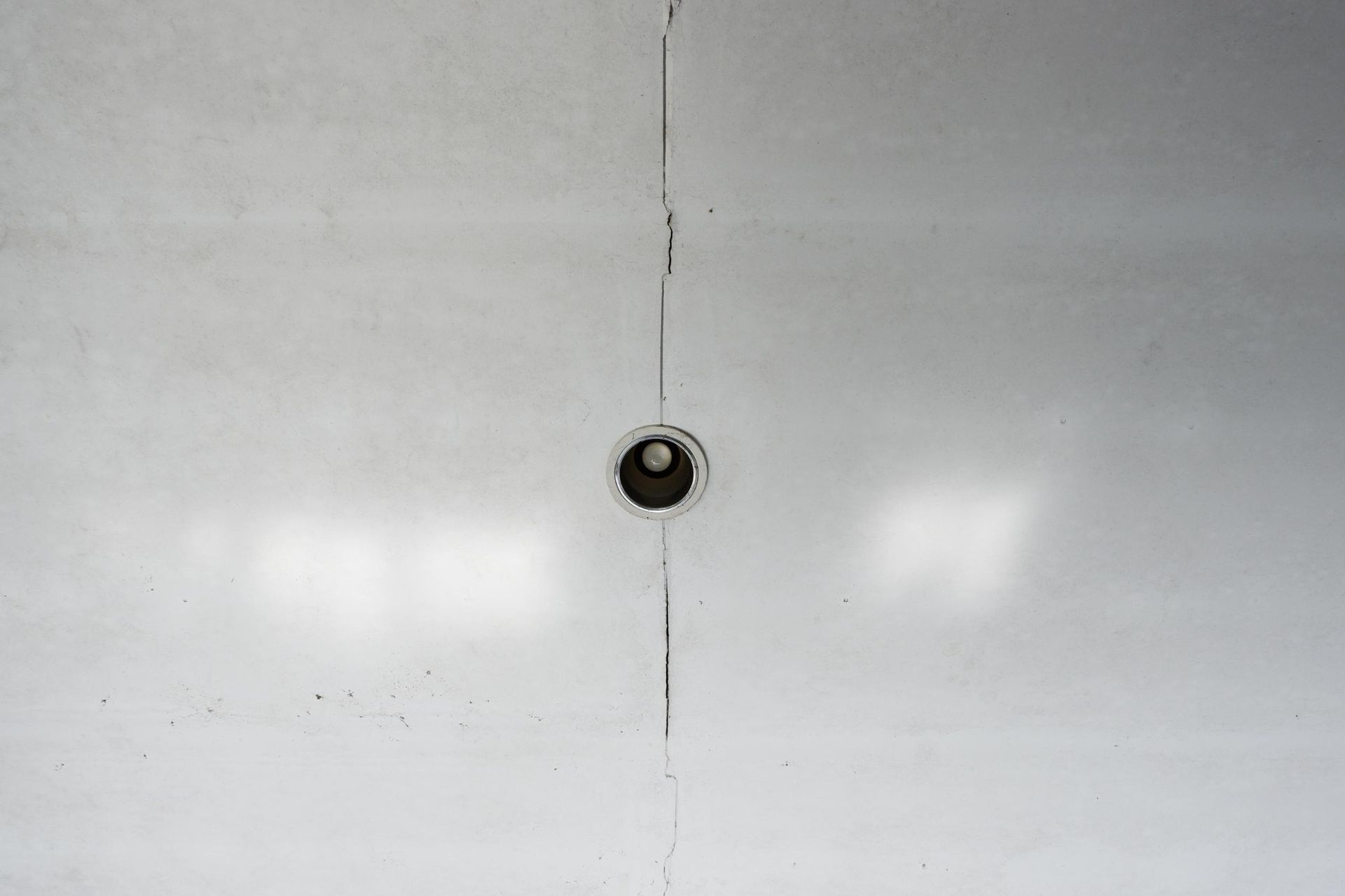White surface with a small, dark circular object in the center. A crack runs vertically through it.