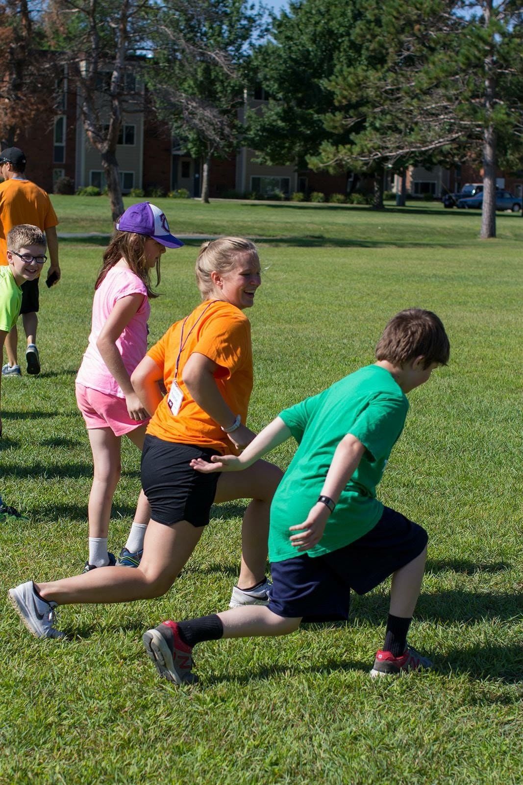 Group of young athletes doing lunges across a grassy field on a sunny day.