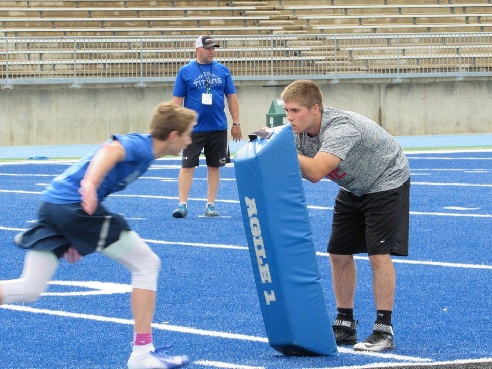 Two young male athletes practicing football drills on a blue football field.