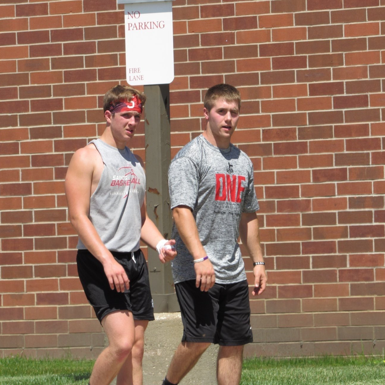 Two college-age male athletes walking outside against brick building.