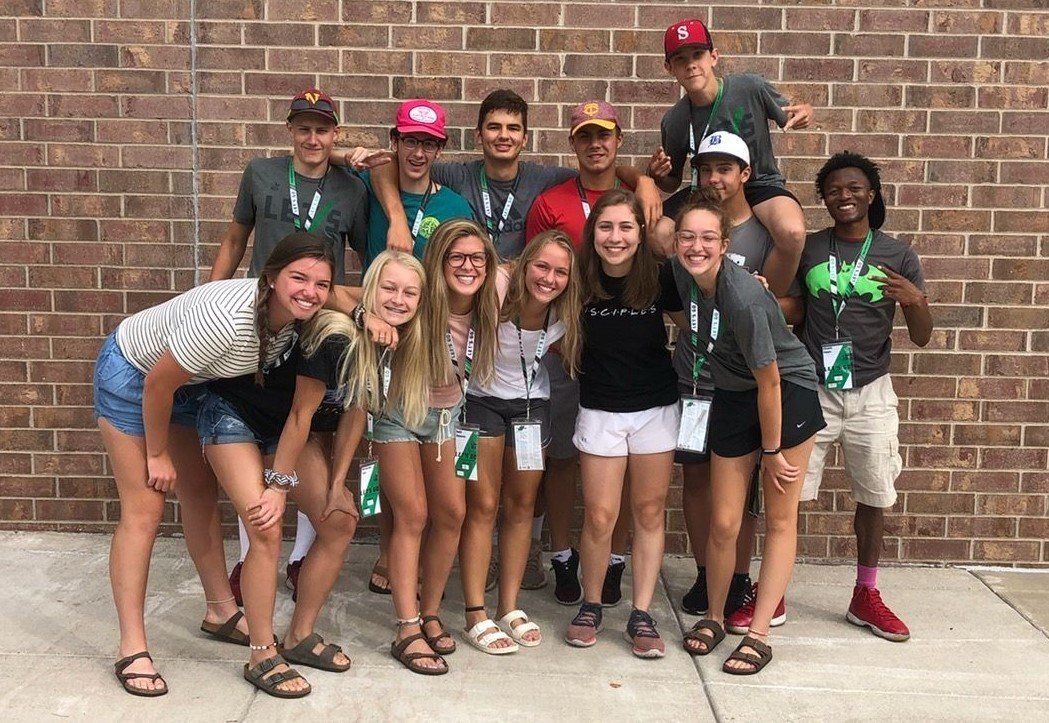 Student athletes in group huddled together smiling at the camera in front of a brick wall.