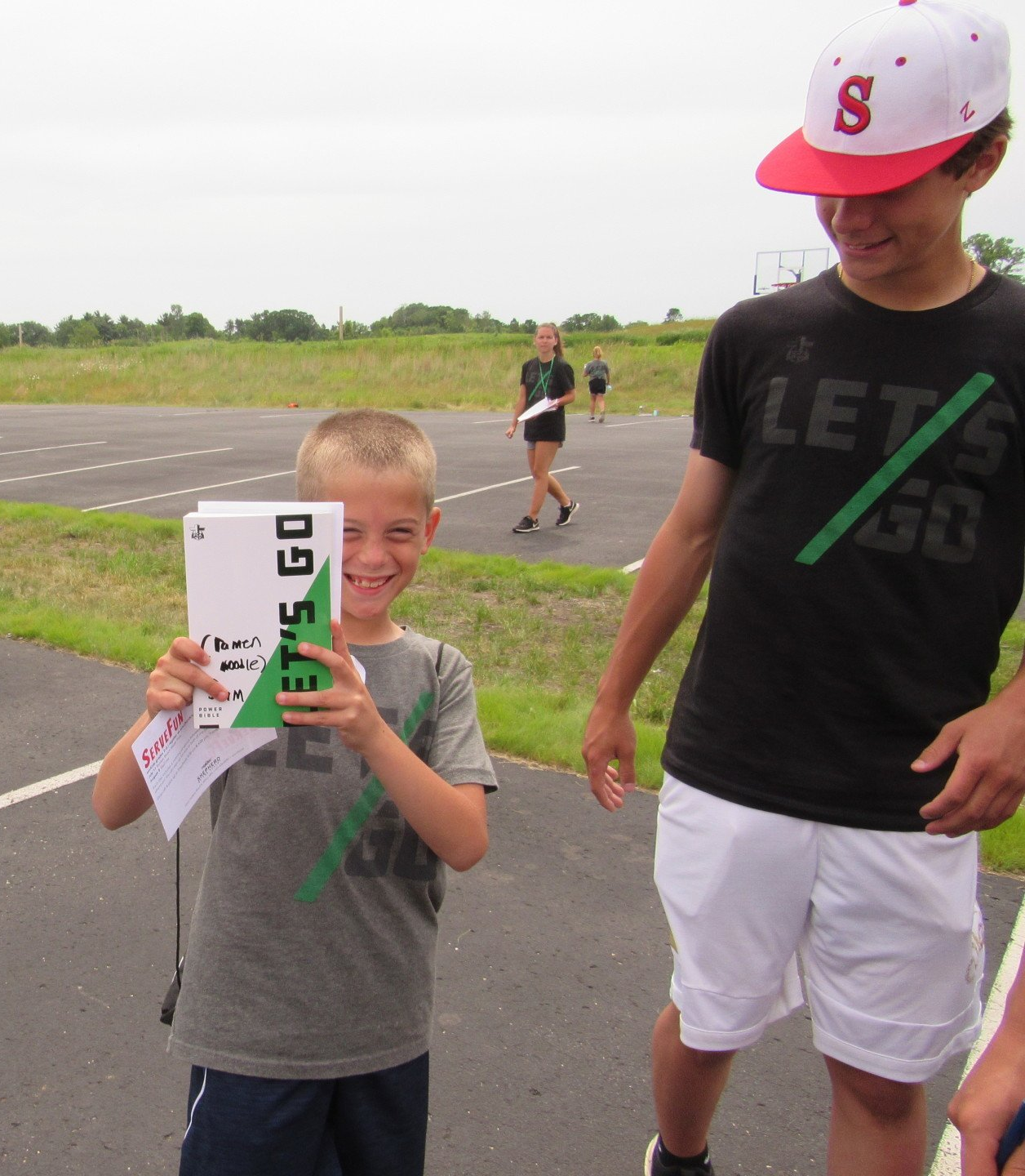 Young boy athlete holding camp flyers that say, 'Let's Go'