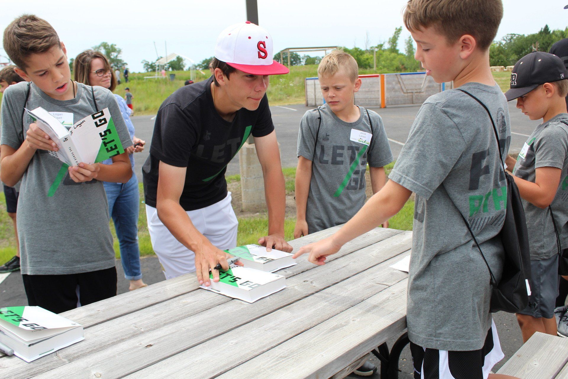 High school leader checking children in for camp at picnic table outside.