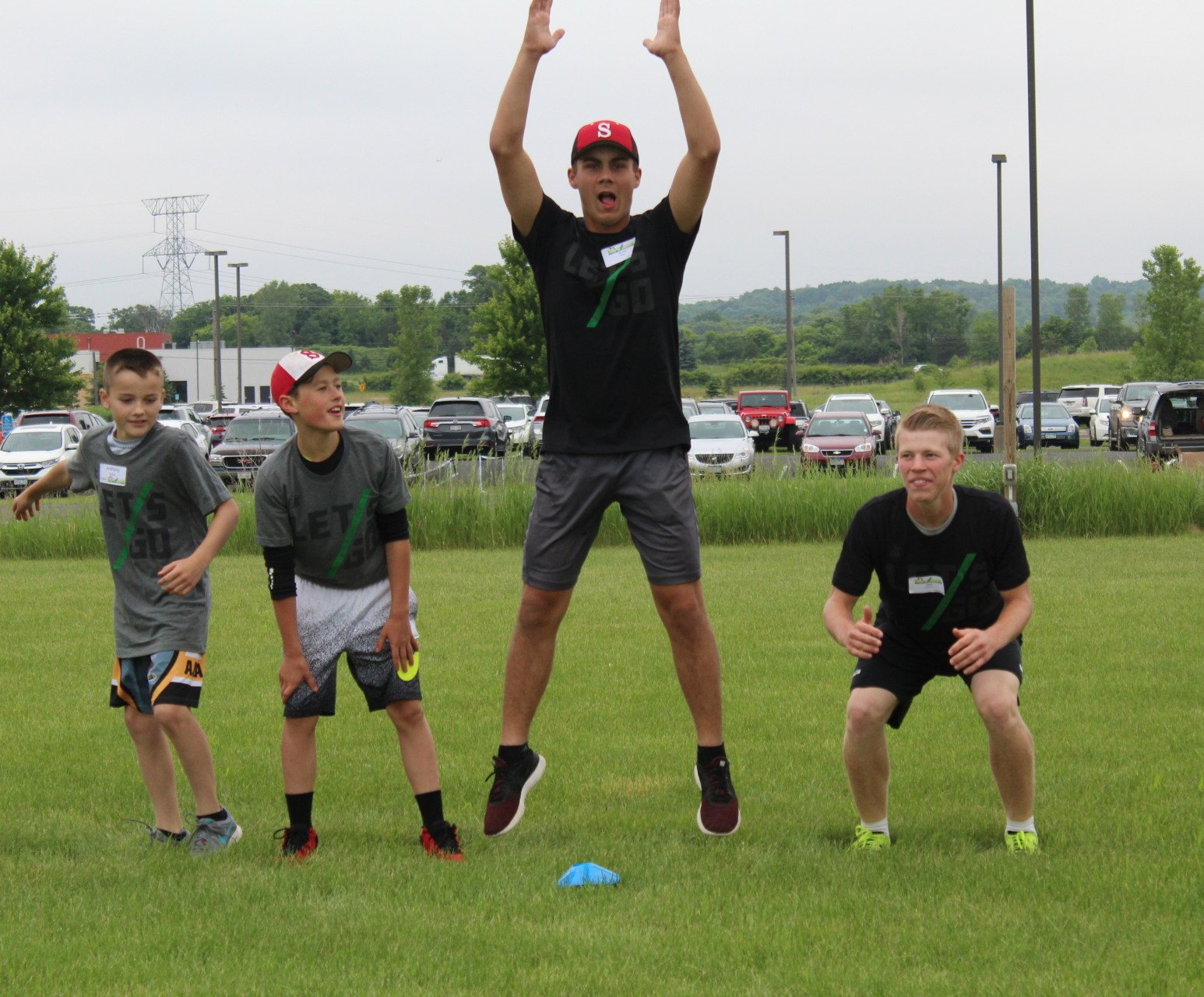 High school leader with young boy athletes doing warm up exercises on field.