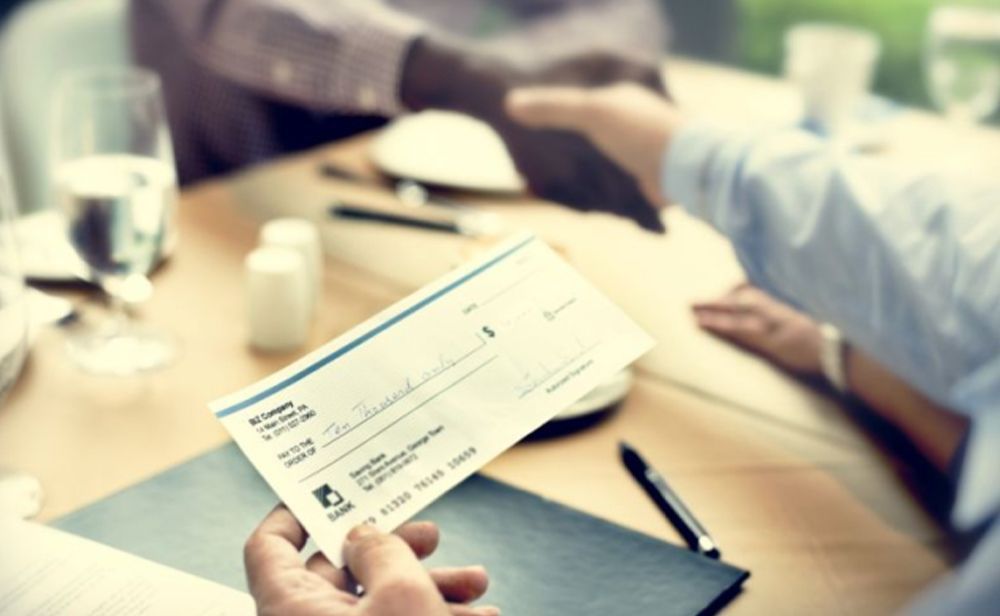 A person is shaking hands with another person while holding a check.