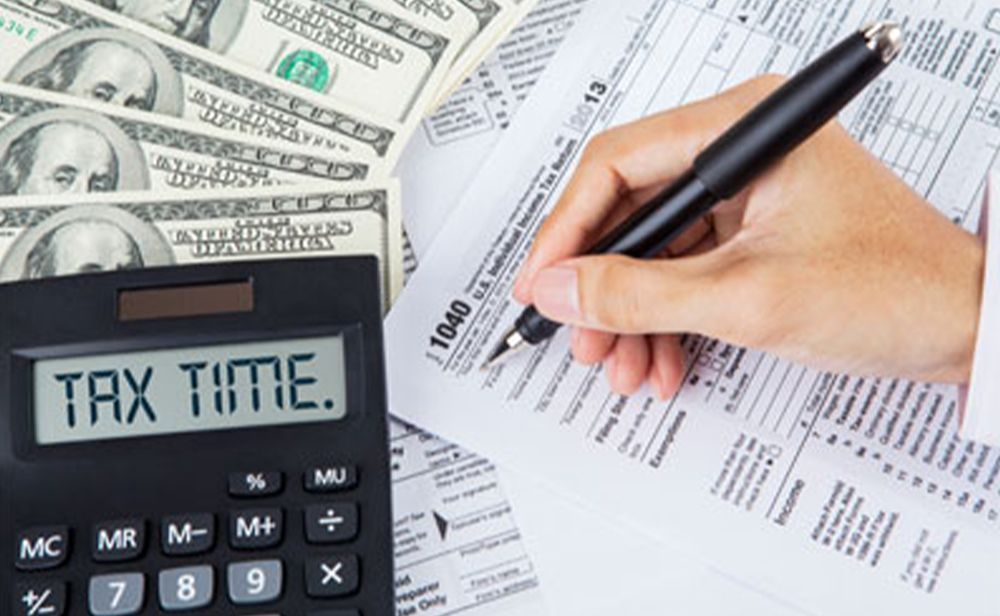 A person is filling out a tax form next to a calculator that says tax time