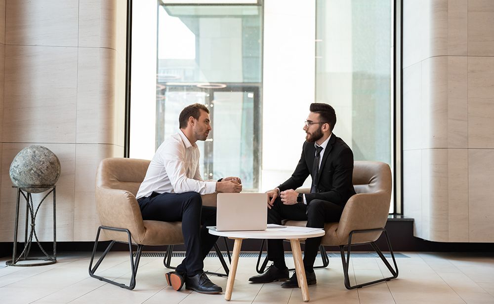 Two men are sitting at a table talking to each other.