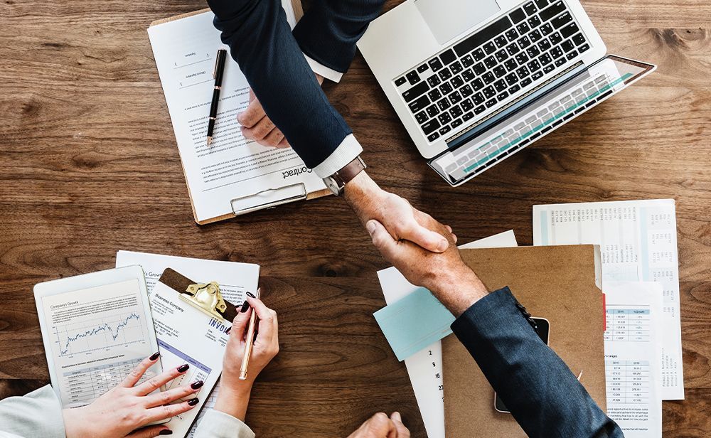 A man and a woman are shaking hands over a wooden table.