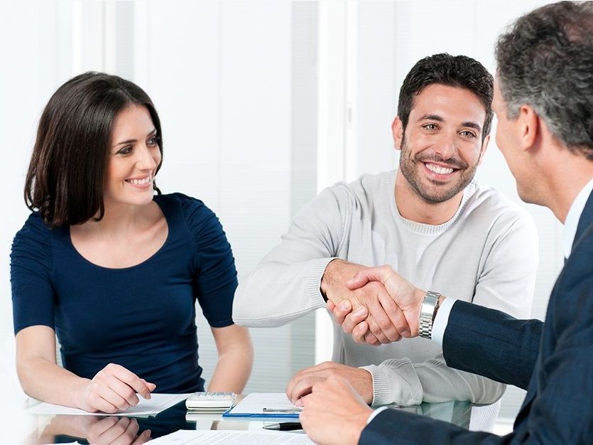 A man and a woman are shaking hands with a man in a suit while sitting at a table.