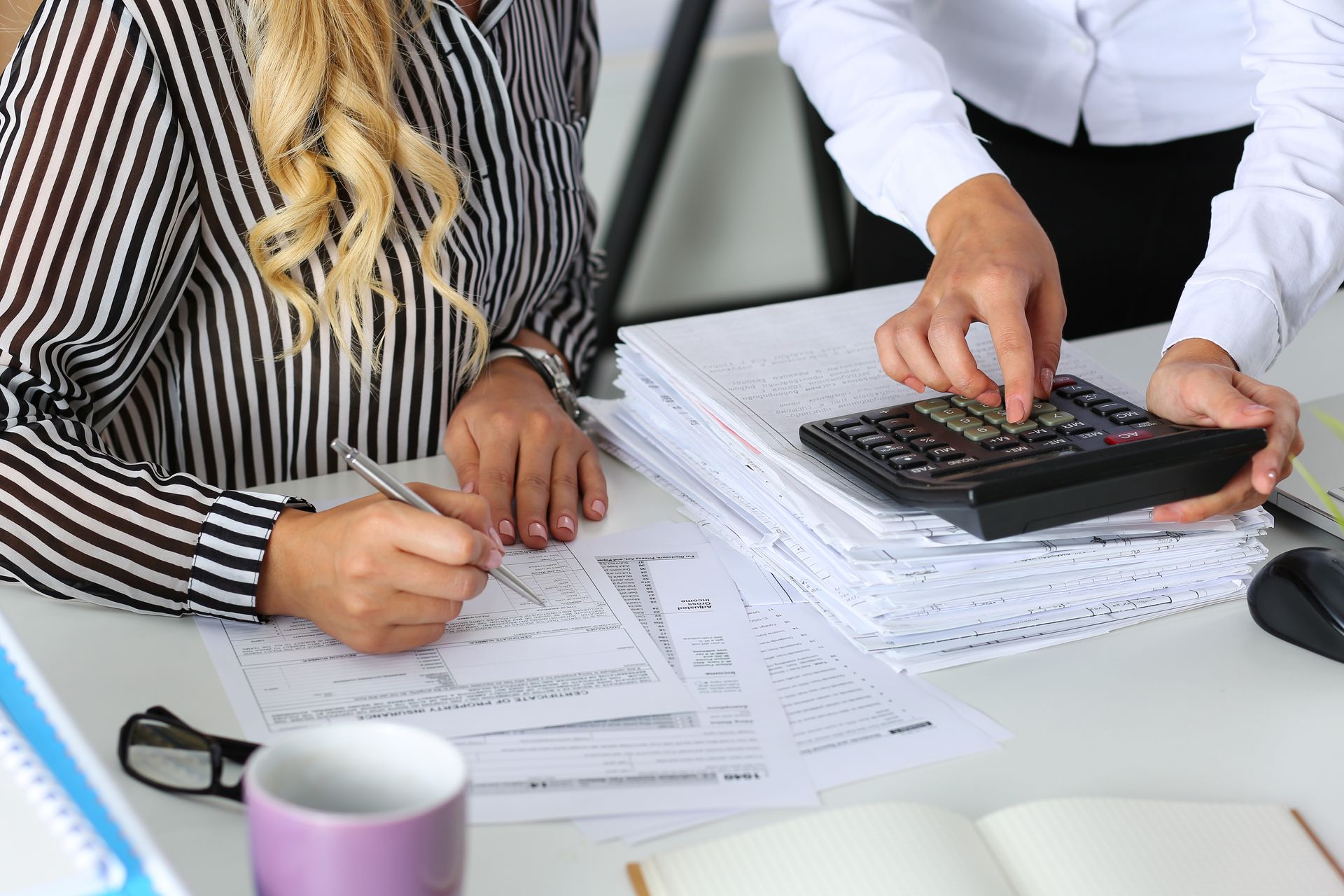 A man and a woman are sitting at a desk using a calculator.