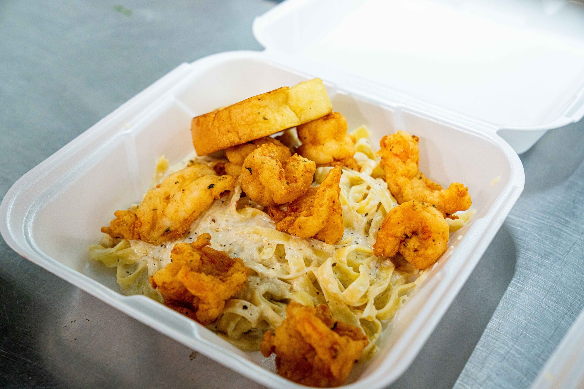 A styrofoam container filled with pasta and shrimp on a table.
