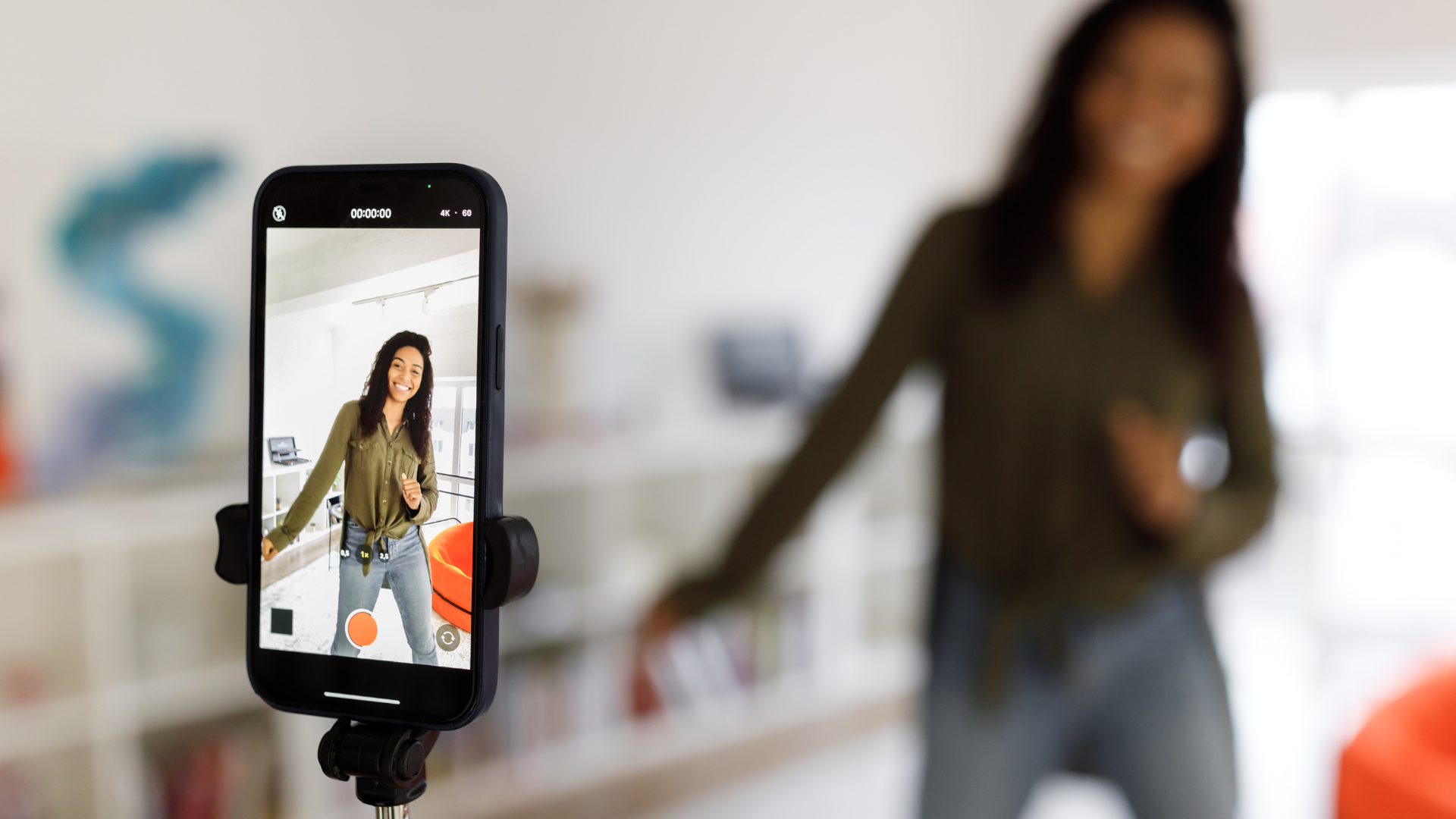 A woman is dancing in front of a cell phone on a tripod.