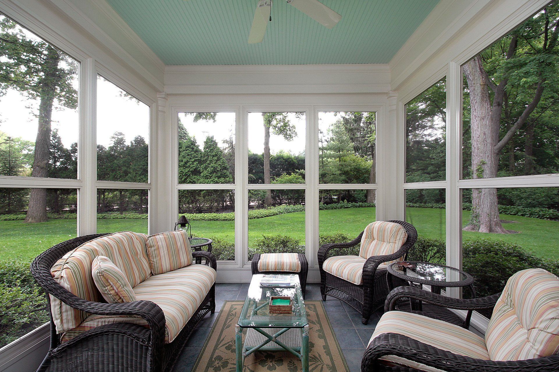 A screened-in porch with a teal ceiling, wicker furniture, and a view of a lush green backyard.