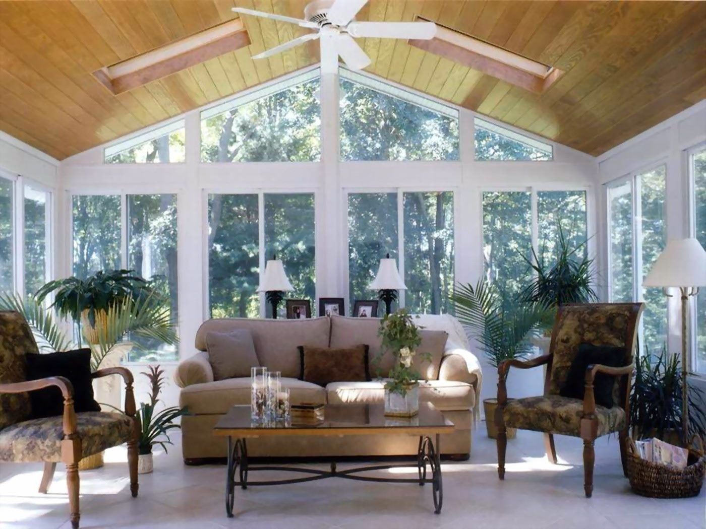 Sunroom with a vaulted wood ceiling, sofa, two armchairs, coffee table, and large windows looking out onto trees.