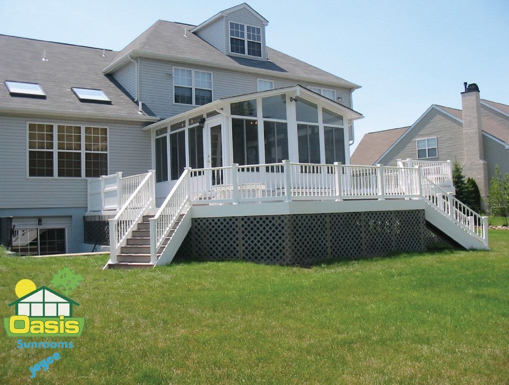 A bright sunroom with a glass dining table, four black metal chairs, light wood floors, and floor-to-ceiling windows.
