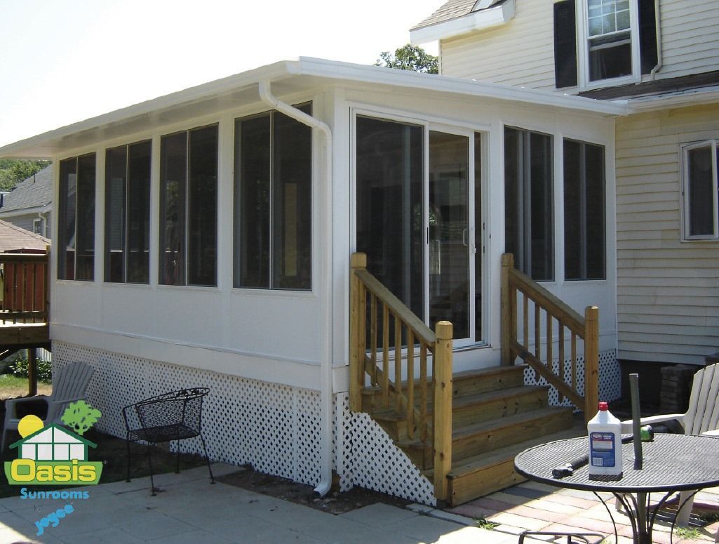 A white sunroom addition attached to a house, featuring large windows, a sliding glass door, and wooden stairs.