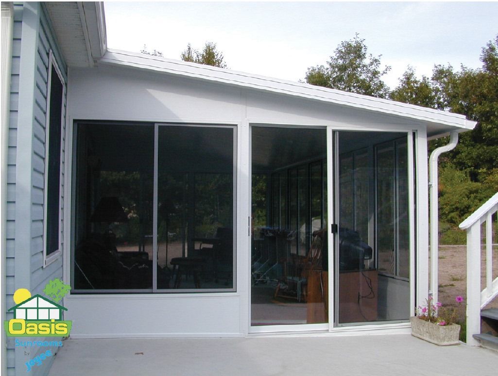 A white sunroom addition featuring glass sliding doors and windows attached to the side of a blue house.