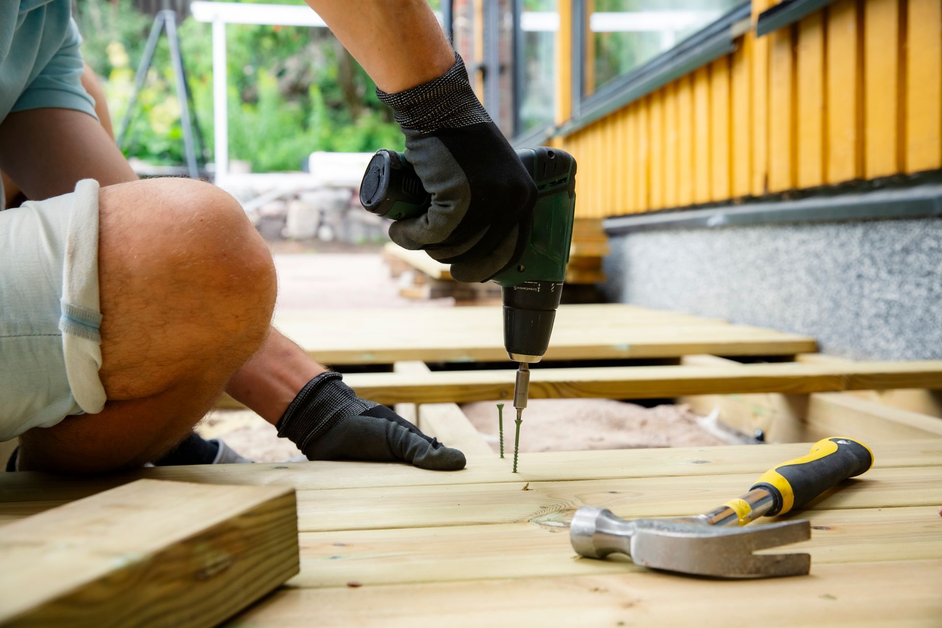 Back view of a house with a large wooden covered patio, a stone fire pit, outdoor seating, and surrounding trees.