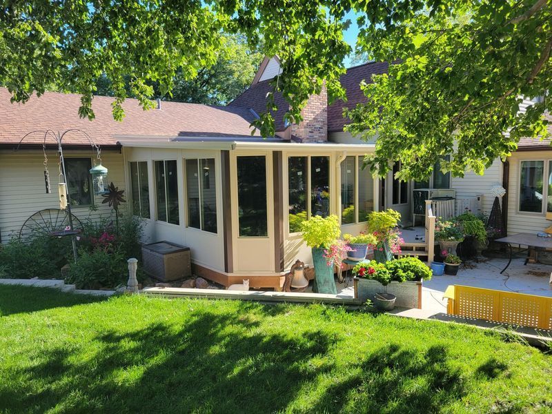 Back view of a house with a large wooden covered patio, a stone fire pit, outdoor seating, and surrounding trees.