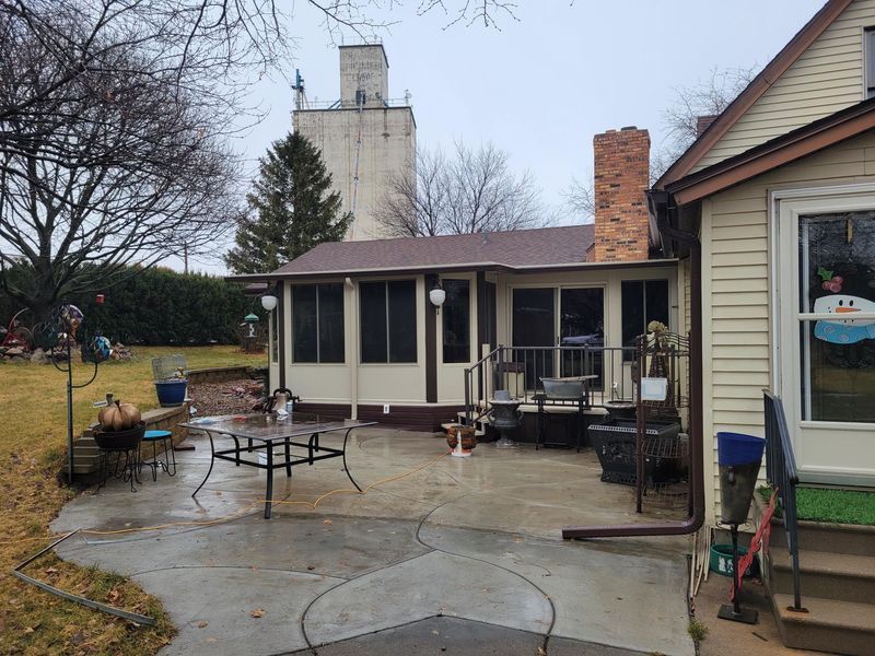 A patio with a table and chairs next to a house with a screened-in porch, with a tall grain silo in the background.