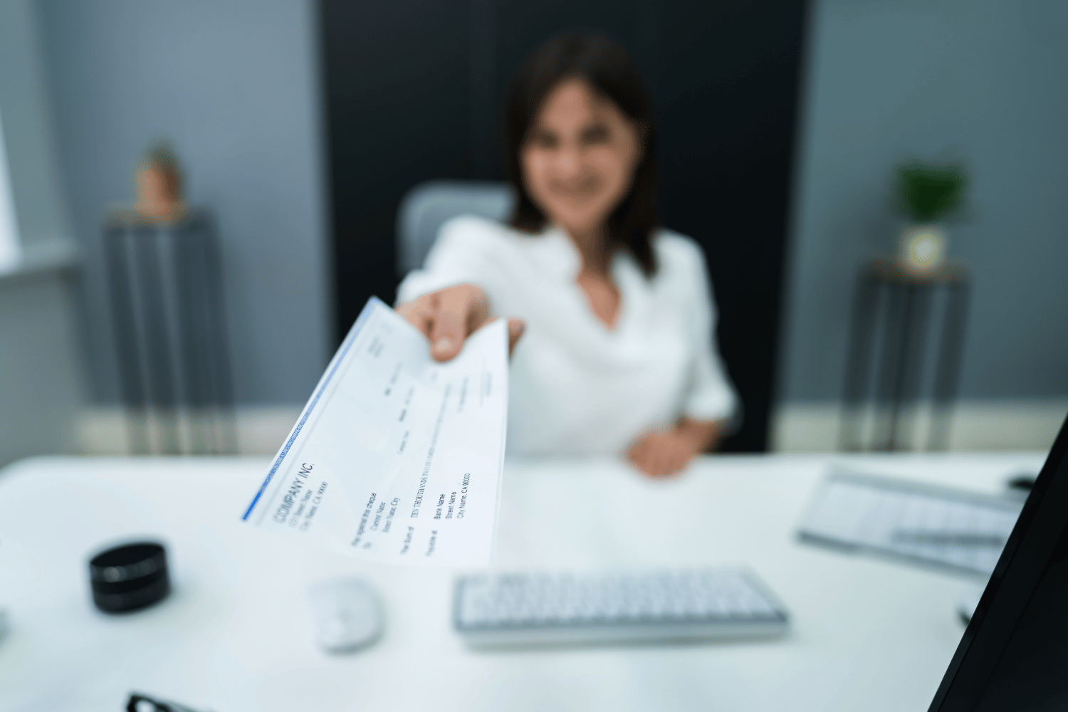 A woman is sitting at a desk holding a check in her hand.