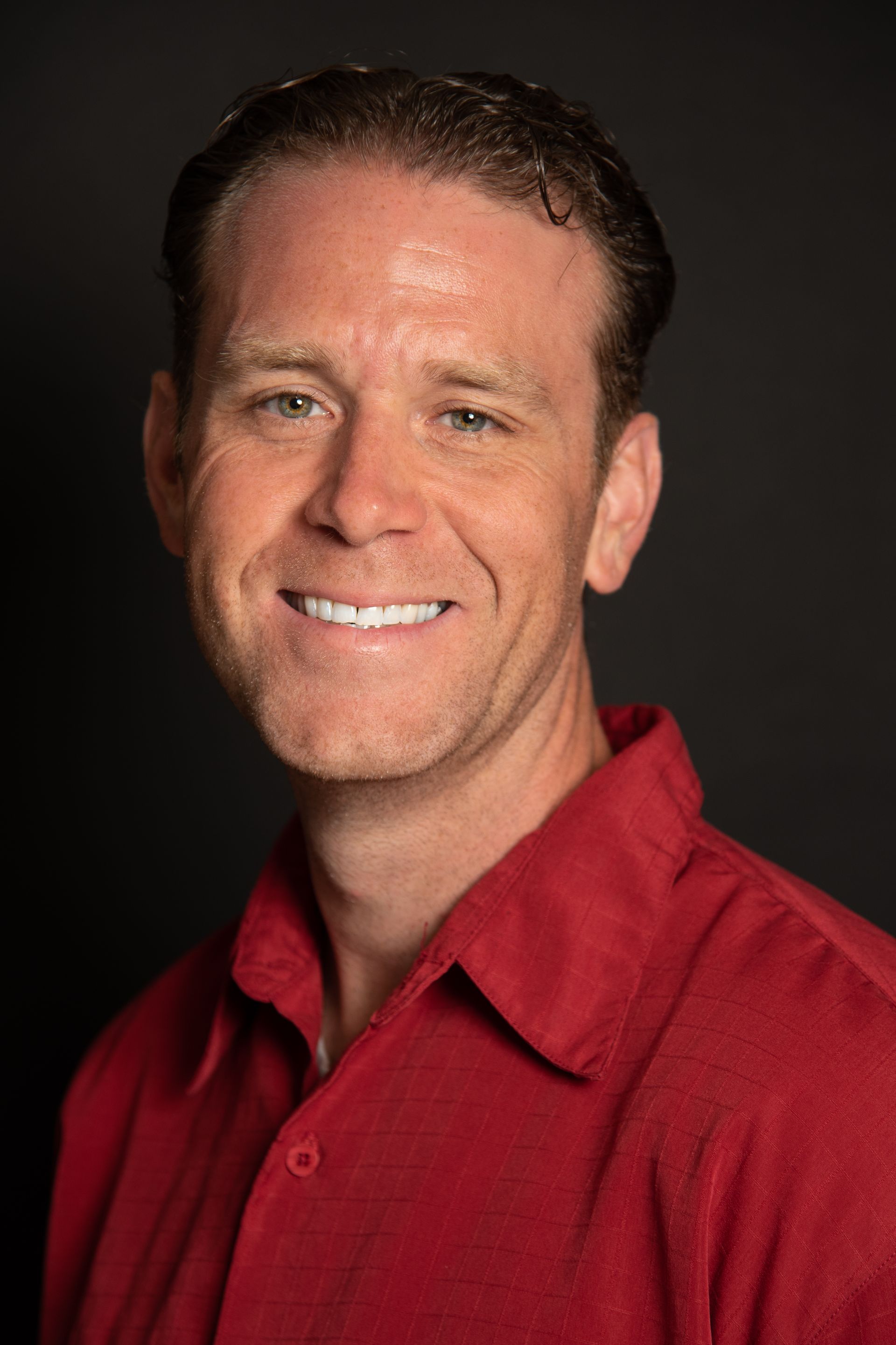 A man in a red shirt is smiling for the camera.