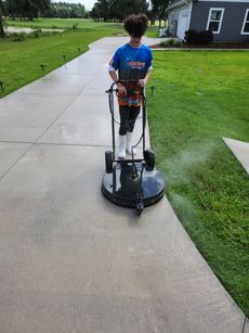 Person using a circular power washer to clean a concrete driveway outside a house.